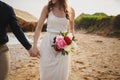 Outdoor beach wedding ceremony near the ocean, close up of hands of stylish couple with wedding bouquet, bride is Royalty Free Stock Photo