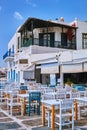 Outdoor cafe or restaurant in typical Greek island town. Church, blue dome, tourists roam. Sunny summer day, Mykonos