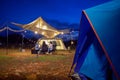 Outdoor camping tent in the forest park, party dinner with friends under tarp or flysheet and warm lighting at night near natural