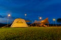 Outdoor camping tent with tarp or flysheet on grass courtyard and warm night light under dark blue sky twilight time, family