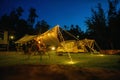 Outdoor camping tent with tarp or flysheet on grass courtyard and warm night light under dark blue sky twilight time, family