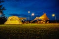 Outdoor camping tent with tarp or flysheet on grass courtyard and warm night light under dark blue sky twilight time, family