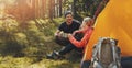 Outdoor camping - young couple resting by a tent with tea cups at forest camp after hiking. active lifestyle