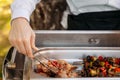 Outdoor catering banquet in summer. Waiter in white shirt puts a barbeque from a chafing dish on a plate. The waiter serves guests Royalty Free Stock Photo
