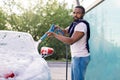 Outdoor cleaning of the car with soap foam using high pressure jet. Handsome bearded African young man washing his red Royalty Free Stock Photo