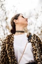 Outdoor close up fashion portrait of young beautiful confident woman with top knot wearing trendy animal, leopard print faux fur Royalty Free Stock Photo