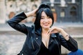 Outdoor close up portrait of young beautiful confident Asian woman, wearing leather jacket, posing on the street of old Royalty Free Stock Photo