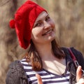 Outdoor close up portrait of young beautiful happy smiling girl wearing french style red knitted beret Royalty Free Stock Photo