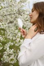 Outdoor close up portrait of young beautiful woman in blooming garden on spring day. Model looking in little mirror, posing in Royalty Free Stock Photo