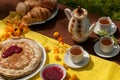 An outdoor composition with tea cups, a tea pot, a plate of pancakes, pastry, ripe fruit and field flowers on a bright table cloth Royalty Free Stock Photo