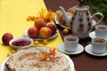 An outdoor composition with tea cups, a tea pot, a plate of pancakes, pastry, ripe fruit and field flowers on a bright table cloth Royalty Free Stock Photo