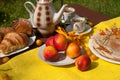 An outdoor composition with tea cups, a tea pot, a plate of pancakes, pastry, ripe fruit and field flowers on a bright table cloth Royalty Free Stock Photo