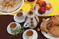 An outdoor composition with tea cups, a tea pot, a plate of pancakes, pastry, ripe fruit and field flowers on a bright table cloth Royalty Free Stock Photo