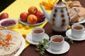 An outdoor composition with tea cups, a tea pot, a plate of pancakes, pastry, ripe fruit and field flowers on a bright table cloth Royalty Free Stock Photo