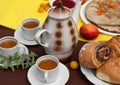 An outdoor composition with tea cups, a tea pot, a plate of pancakes, pastry, ripe fruit and field flowers on a bright table cloth Royalty Free Stock Photo