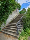 Outdoor concrete stairway with forger decorative iron handrails and ivy covered wall. Sunny summer day, no people