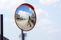 Outdoor convex safety mirror hanging on wall with reflection of an urban roadside view of cars parked along the street