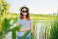 Outdoor country portrait of teenage girl in hat sunglasses near pond in the reeds Royalty Free Stock Photo