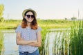 Outdoor country portrait of teenage girl in hat sunglasses near pond in the reeds Royalty Free Stock Photo