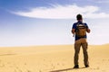 Outdoor desert adventure and alternative tourism and tourist activity with standing man from back with backpack looking a sand Royalty Free Stock Photo