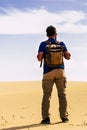 Outdoor desert adventure and alternative tourism and tourist activity with standing man from back with backpack looking a sand Royalty Free Stock Photo