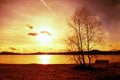 Outdoor empty bench on autumn lake beach. The coast with sunset. Vintage toned photo with lens flare effect Royalty Free Stock Photo