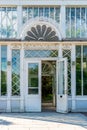 Outdoor facade front view of an old white ornamented glass greenhouse entrance with open door.