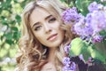 Outdoor fashion beautiful young woman surrounded by lilac flowers summer. Spring blossom lilac bush. Portrait of a girl blond Royalty Free Stock Photo