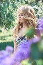 Outdoor fashion beautiful young woman surrounded by lilac flowers summer. Spring blossom lilac bush. Portrait of a girl blond Royalty Free Stock Photo