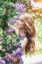 Outdoor fashion beautiful young woman surrounded by lilac flowers summer. Spring blossom lilac bush. Portrait of a girl blond Royalty Free Stock Photo