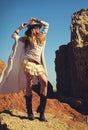 Outdoor fashion photo of young happy woman in hat, sitting on a fur against rocks, hands up Royalty Free Stock Photo