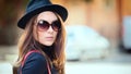 Outdoor fashion portrait of smiling young woman wearing trendy black hat and big retro sunglasses