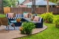 Outdoor furniture - striped sectional on round patio with area rug and chair and ferns with trees and neighboring houses in Royalty Free Stock Photo