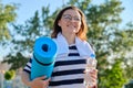 Outdoor happy mature woman walking after fit exercises in park, with backpack, yoga mat Royalty Free Stock Photo