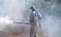 Outdoor healthcare worker using fogging machine spraying chemical to eliminate mosquitoes in public area