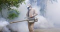 Healthcare worker using fogging machine spraying chemical to eliminate mosquitoes on overgrown at slum area