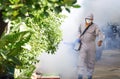 Outdoor healthcare worker spraying chemical to eliminate mosquitoes on overgrown in slum area