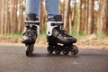 Outdoor horizontal picture of black and white roller skates being on road over tree background in forest, having ride, sticking to