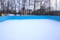 An outdoor ice skating rink and a hockey net with tall frost covered trees in the background in a winter landscape