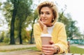 Outdoor image of pretty woman drinking coffee at terrace cafetaria in the park. Female in the city street drinking hot cappuccino