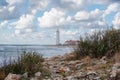 Outdoor landscape with sea stormy rocky shore and white beacon on horizon with beautiful clouds