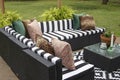 Outdoor lawn furniture with black and white crisply striped upholstery and assorted pillows grouped around a table with ferns on a