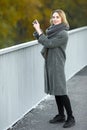 Outdoor lifestyle photo of young beautiful blonde woman in fall autumn park taking photos on smartphone cozy scarf grey vintage co Royalty Free Stock Photo