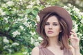 Outdoor lifestyle photo of young beautiful lady. Brown hair, fedora hat. Perfect face on blossoms flowers background Royalty Free Stock Photo