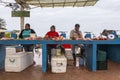 Outdoor male and female fish vendors seen sitting behind their products next to sea lion and pelicans