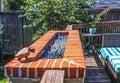 Outdoor natural gas fire pit with low flames on patio with privacy fence in background and colorful seating