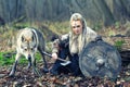 Outdoor northern warrior woman with braided hair and war makeup holding shield and ax with wolf next to her ready to attack -