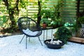 Outdoor patio furniture on pebbles in a front garden. Front veranda of house with two black Acapulco armchairs, coffee table and p
