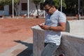 Outdoor photo of a charismatic young student with sunglasses using a smartphone A Latino man smiling as he surfs the social