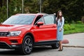 Outdoor photo of gorgeous woman posing near orange suv car .